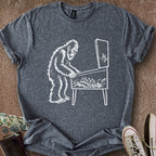 Printify T-Shirt Dark Heather / S 0182_bigfoot playing pinball T-Shirt